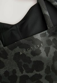 Crni aktivni gornji dio odjeće s teksturiranim uzorkom leopard printa i riječi "ACTIVE" u modernom i elegantnom fontu na prednjoj strani.