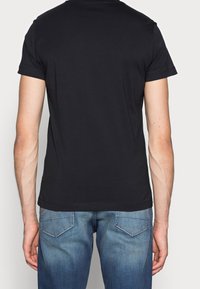 Svart kortärmad skjorta med rund halsringning, tillverkad av mjukt bomullstyg, ihop med blekta blå jeans med en klassisk femfickdesign.