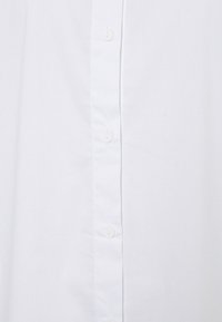 Camisa blanca de algodón con botones que cuenta con una tapeta vertical con seis botones blancos y una textura lisa y uniforme.