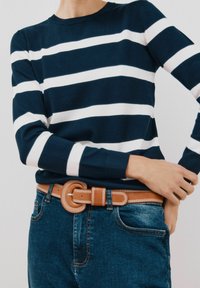 Maglione a righe blu navy e bianche con maniche lunghe e scollatura rotonda, abbinato a jeans blu a vita alta e una cintura in pelle chiara con fibbia rotonda.