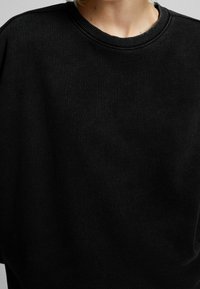 Sudadera negra con cuello redondo. Presenta una tela texturizada y un cuello acanalado. Diseño simple y sin adornos.