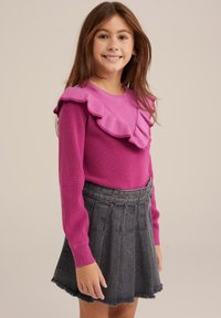 Pink knitted sweater with ruffled neckline, paired with a dark gray denim pleated skirt featuring a frayed hem.