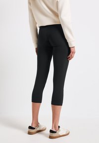 Svarta capri leggings med en figursydd design, tillverkade av stretchigt material, med en jämn yta och längd till mitten av vaden. Bärs med ljusa sneakers.