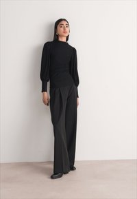 Black long-sleeve top with puff shoulders and ruched side detail, paired with high-waisted, wide-leg trousers in a coordinating shade.