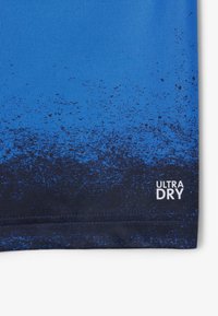 Blå gradient idrottströja, texturerad tyg med ett fadermönster till mörkblått. Har en "ULTRA DRY"-etikett i vitt på den nedre kanten.