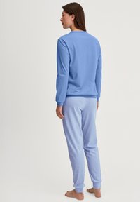 Blaues Langarmoberteil und gestreifte Schlafanzughose. Das Oberteil hat ein einfaches Design, während die Hose vertikale blau-weiße Streifen aufweist.