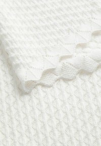 Tissu tricoté blanc avec des motifs de dentelle complexes, des bords festonnés et un design texturé et plié.