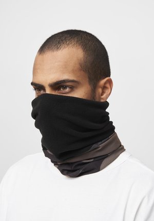 Man with short hair wearing black fleece neck gaiter covering nose and mouth, layered over patterned scarf and white shirt, facing left.