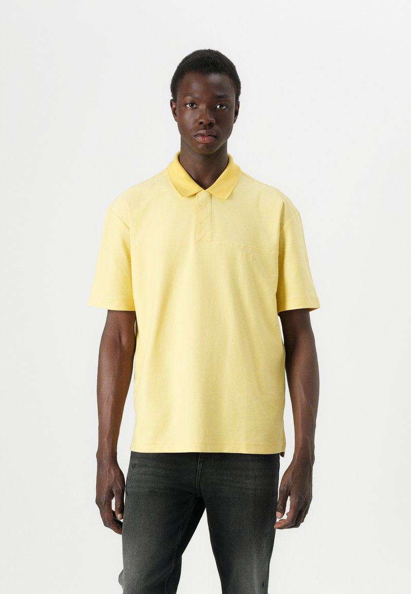 Gul polo-skjorte laget av bomull, med klassisk krage, korte ermer og en liten logo på brystet. Bært med mørke jeans.