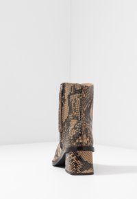 Botín de cuero con estampado de piel de serpiente marrón y negro, con una cremallera en el lateral y un tacón grueso de altura media, visto desde atrás.
