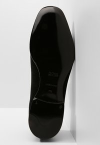 Semelle de chaussure en daim noir avec une finition lisse, marquée du nom de la marque et de la taille. Présente une forme arrondie et des détails de couture subtils.