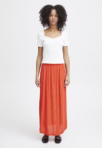 Vit ribbad kortärmad topp med fyrkantig ringning, ihop med en flödande orange maxikjol. Svarta platta skor fulländar outfiten.