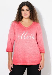 Top lungo a maniche lunghe ombre rosso con scollatura a V e maniche a 3/4. Presenta il testo "Moin" in corsivo bianco, tessuto morbido con una leggera trama.