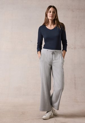 Mörkblå långärmad topp med V-hals tillsammans med ljusgrå vida sweatpants. Byxorna har fickor och dragsko i midjan. Vita sneakers.