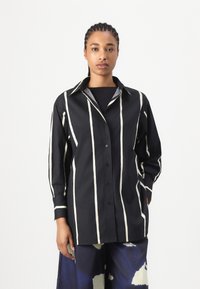 Black button-up shirt with white vertical stripes, featuring a collar and long sleeves. Smooth fabric texture, minimalistic design.