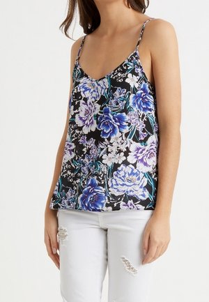 Camiseta negra de flores con tirantes ajustables, que presenta flores azules y moradas sobre un fondo en contraste. Se lleva con pantalones blancos desgastados.