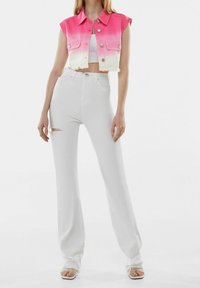 Gilet di jeans in ombre rosa con bottoni frontali e due tasche sul petto, abbinato a jeans bianchi a vita alta a zampa d'elefante con dettagli strappati sul davanti.