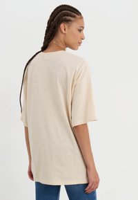 Beige oversized t-shirt van zachte stof, met korte mouwen en een ronde halslijn. Heeft een relaxte pasvorm en eenvoudige stikseldetails.