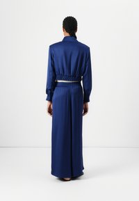 Robe longue en satin bleu marine avec une taille cintrée, des manches longues et un col, présentant une texture lisse et une coupe décontractée.