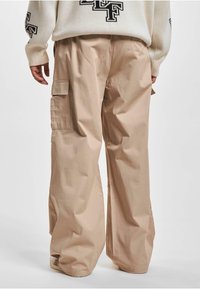 Pantaloni cargo bej cu picioare late, având o textură ușoară, dotati cu buzunare laterale și o croială relaxată, concepuți pentru confort și utilitate.
