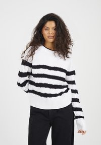 Sweter dzianinowy w białym kolorze z czarnymi poziomymi paskami, z teksturowanym wzorem oraz ściągaczami u dołu i na mankietach. Wykończenie w stylu crew neck.