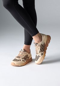 Zapatillas beige con acentos de estampado de leopardo, parte superior texturizada y una suela gruesa de color marrón claro. Atadas con detalles tonales adicionales y costuras.