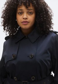 Tengerészkék ballonkabát kétrétegű, dupla gombsoros kialakítással, nagy gombokkal és övvel. Klasszikus gallérral és sima, texturált anyagból készült.