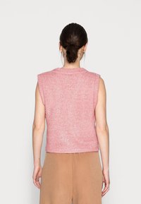 Top court sans manches en rose clair, en tissu texturé avec un léger éclat. Bords bruts aux manches et à l'ourlet. Assorti avec un pantalon beige.