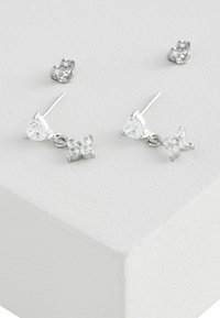 Orecchini a perno in tono argento con accenti di pietre trasparenti, caratterizzati da un piccolo design a fiocco e una finitura liscia. Inclusi chiodini a farfalla.