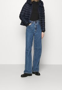 Giacca imbottita blu navy con cappuccio, maglietta nera a maniche lunghe, jeans blu a vita alta e stivaletti neri alla caviglia. Il denim è ampio con gamba dritta.