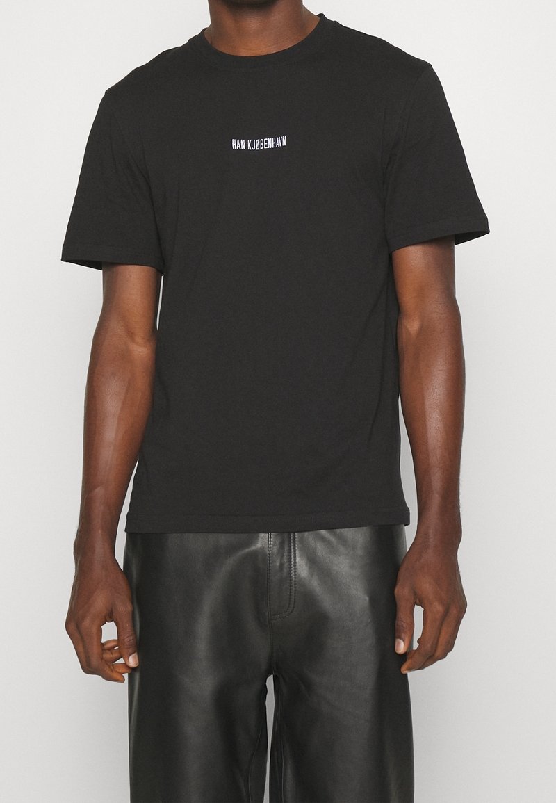 Man wearing a black short-sleeve t-shirt with white "HAN KJØBENHAVN" text centered on chest and black leather pants.