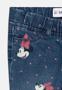 Jeans de mezclilla de color azul oscuro con lunares rosas y un diseño repetido de Minnie Mouse con un lazo rojo. Incluye una cinturilla elástica.
