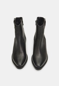 Botines de cuero negro hasta el tobillo con punta afilada, textura suave y cierre de cremallera lateral. Diseño minimalista con detalles de costura sutiles.