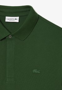 Polo de algodón verde con cuello de canalé, presenta una tapeta de dos botones y un logo de cocodrilo bordado en el lado izquierdo del pecho.