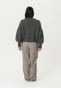 Pull en maille grise avec un tissu texturé, des manches surdimensionnées et des poignets côtelés, associé à un pantalon beige clair, large et confortable.