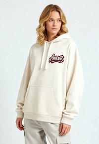 Hoodie crema con tasca frontale, logo ricamato "Amour" in rosso e nero, cappuccio con coulisse, polsini e orlo a coste. Tessuto in cotone morbido.