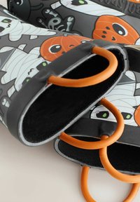 Bottes de pluie en caoutchouc noires avec des motifs d'Halloween, comprenant des momies, des citrouilles et des squelettes ; poignées orange et intérieur texturé noir.