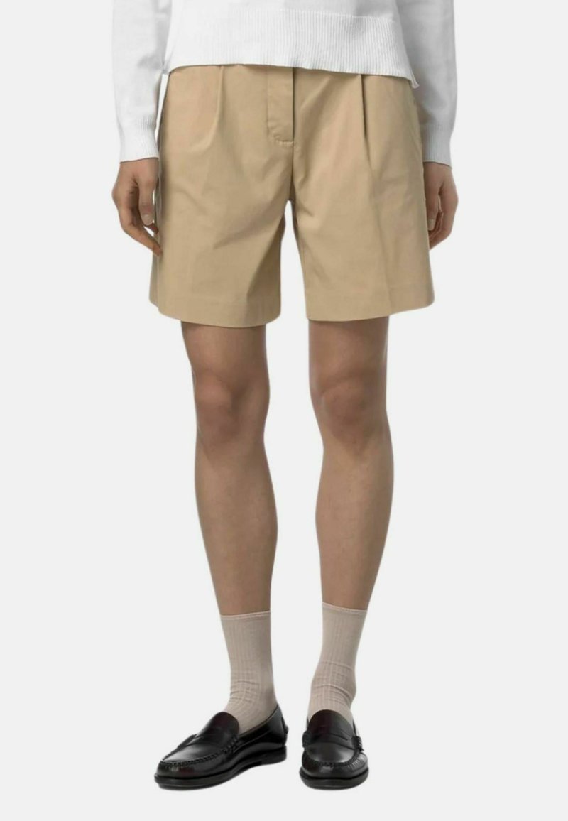 Pantaloni corti in cotone beige con pieghe, caratterizzati da un design a taglio dritto. Abbinati a mocassini neri e calzini chiari.