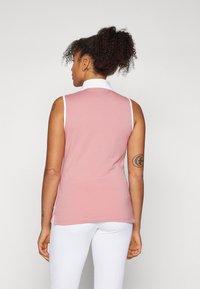 Ermeløs rosa polo skjorte med hvit krage, med en jevn tekstur og sideslits. Bakfra viser den en tettsittende design.