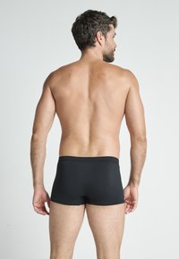 Black cotton boxer shorts with an elastic waistband, featuring a smooth texture and simple design. Model shown from the back.