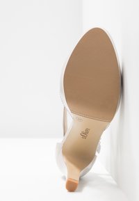 Chaussure à talons hauts beige avec un extérieur en daim lisse, un bout pointu, et une semelle en caoutchouc tan robuste dotée d'une texture antidérapante et du logo de la marque.