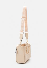 Beige laukku, jossa on tikattu pinta ja kiiltävä viimeistely, kaksinkertaiset kultaiset kahvat ja säädettävä hihna, jossa on "RIVER ISLAND" -teksti. Mukana koristeellinen charm.
