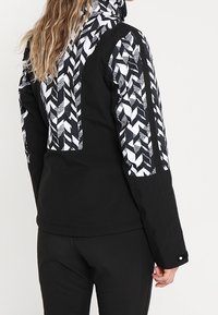 Czarna kurtka z geometrycznym, czarno-białym wzorem na górnej części pleców i rękawach, z wysokim kołnierzem i długimi rękawami.