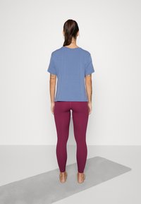 Modrá tričko s krátkým rukávem, volného střihu, kombinované s leggings ve vínové barvě s vysokým pasem. Hladká textura a minimální designové detaily.