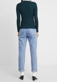 Morski prążkowany top z długim rękawem w połączeniu z jasnoniebieskimi, wysokim stanem jeansami, z podwiniętymi mankietami oraz białymi botkami na blokowym obcasie.