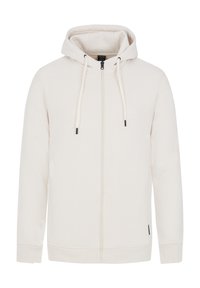 Felpa con zip di un beige chiaro realizzata in tessuto morbido, dotata di cappuccio regolabile con cordino, polsini elasticizzati e una piccola etichetta decorativa sull'orlo.