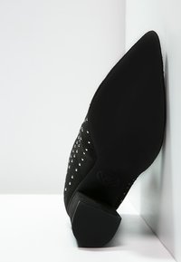 Schwarzer High-Heel-Schuh aus Wildleder mit spitzer Zehenpartie, verziert mit silbernen Nieten, mit einer strukturierten Sohle und einem glatten Absatz.