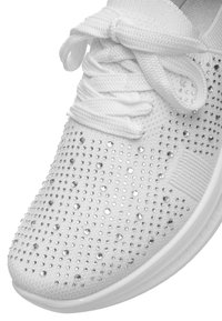 Punta di una sneaker bianca con spesse stringhe bianche e piccoli borchie d'argento incastonate nella tomaia in tessuto.