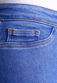 Jeans de mezclilla azul con un pequeño bolsillo trasero, costuras en un tono amarillo-naranja contrastante y una tela de textura suave.