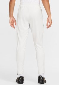 Hvide atletiske bukser med tapered fit, elastisk talje, lynlåsdetaljer ved anklene, og sidelomme. Bæret med sort og guld fodtøj.